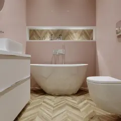 Elegancka łazienka z wolnostojącą wanną i baterią natynkową wannową. Jasne płytki i drewniana podłoga tworzą przytulną atmosferę.