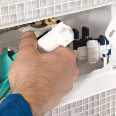 Dłoń montuje mechanizm spłuczki podtynkowej w białej obudowie. Widoczne elementy hydrauliczne i zielony zbiornik.