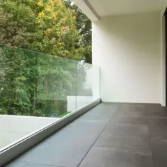 Nowoczesne płytki na balkon w bloku, z widokiem na zielony ogród i szklaną balustradę.