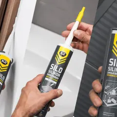 Ręce trzymają tuby z silikonem. Jeden z nich to silikon bezbarwny sanitarny, idealny do łazienek.